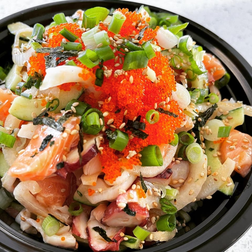Close-up of a vibrant Poki Bowl with salmon, octopus, roe, cucumbers, and green onions.