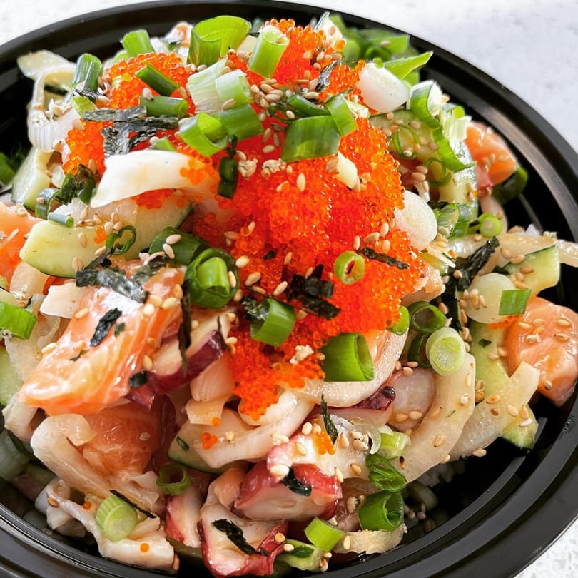 Close-up of a vibrant Poki Bowl with salmon, octopus, roe, cucumbers, and green onions.