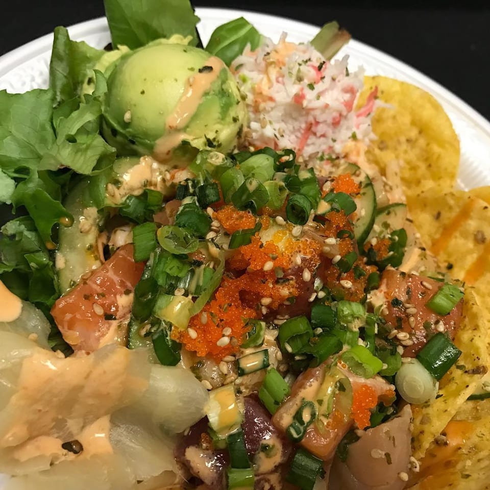 A vibrant Poki Bowl with salmon, avocado, crab salad, roe, green onions, and tortilla chips.