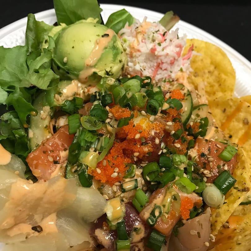 A vibrant Poki Bowl with salmon, avocado, crab salad, roe, green onions, and tortilla chips.