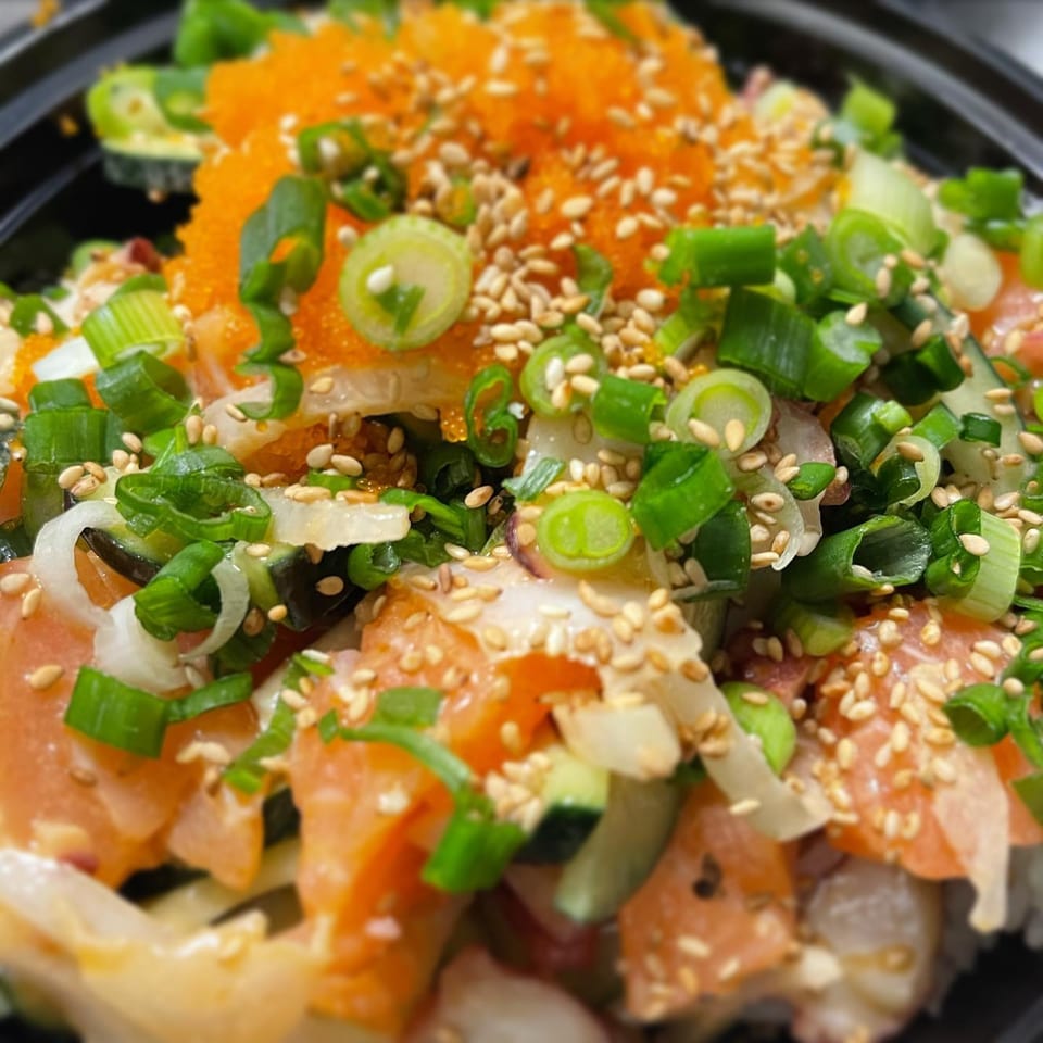 Close-up of a Poki Bowl with salmon, roe, green onions, sesame seeds, and other toppings.
